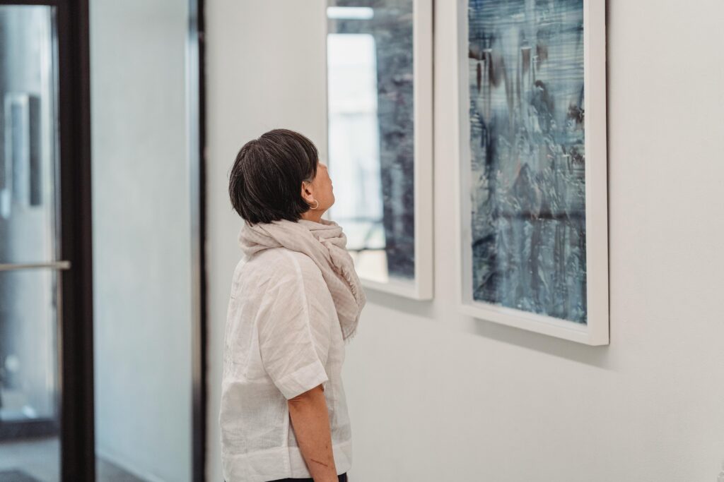 A woman in a gallery intently observes abstract paintings, highlighting her engagement with modern art.